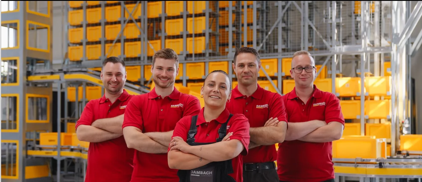 Team in roter Arbeitskleidung vor einem automatisierten Hochregallager