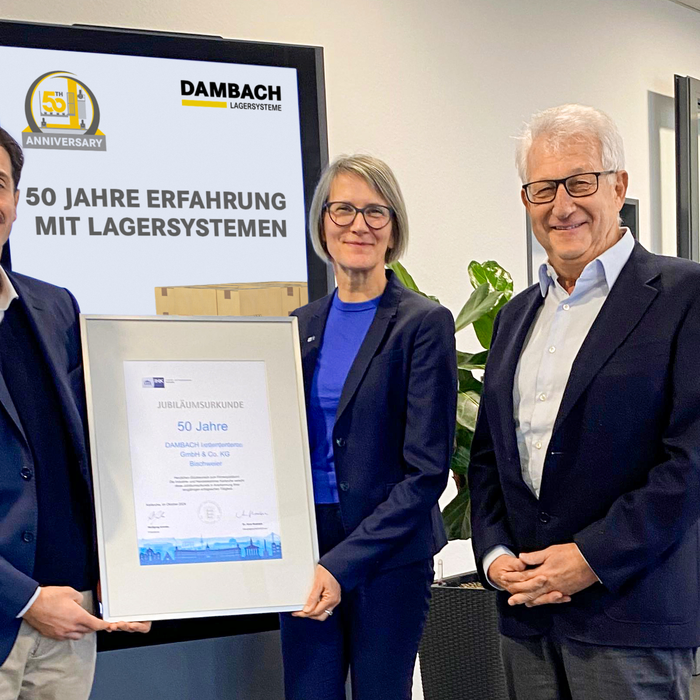 Drei Personen präsentieren gemeinsam die 50 Jahre DAMBACH Urkunde in einem Büro